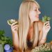 A smiling woman holding avocado and basil, surrounded by fresh vegetables and fruits for healthy eating.