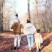 A family of four strolling on a leaf-covered path in a fall forest.