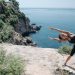 A woman in activewear stretches on a cliff by the ocean, embracing coastal fitness.